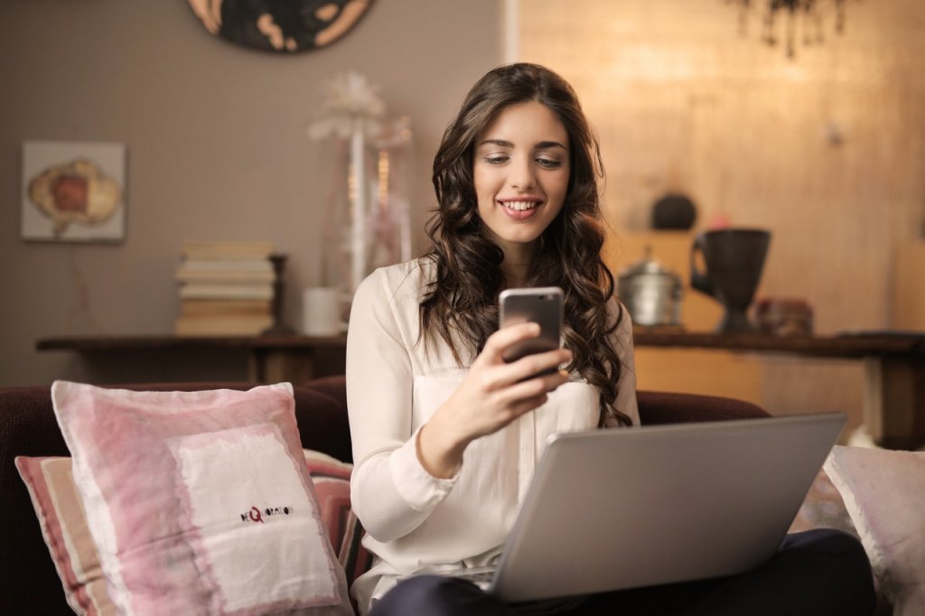 Persona trabajando su negocio desde su casa con su página web en la computadora y su celular en tiempos de pandemia.